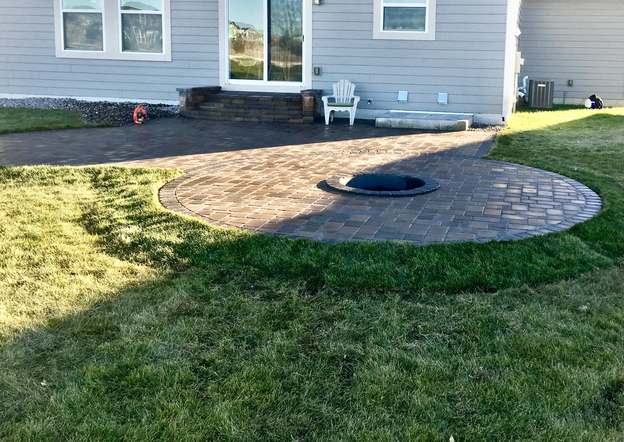Completed paver patio, steps, and lawn forming connected outdoor living zones by Elzo Landscape